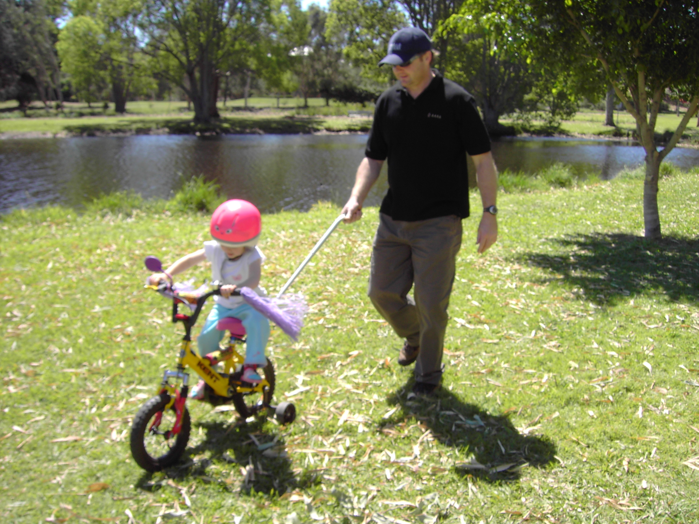 Parent guiding a toddler on a trike using the Push Me Home handle during a family ride.